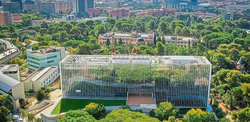 Vista aérea edificio rodeado de árboles en ciudad.