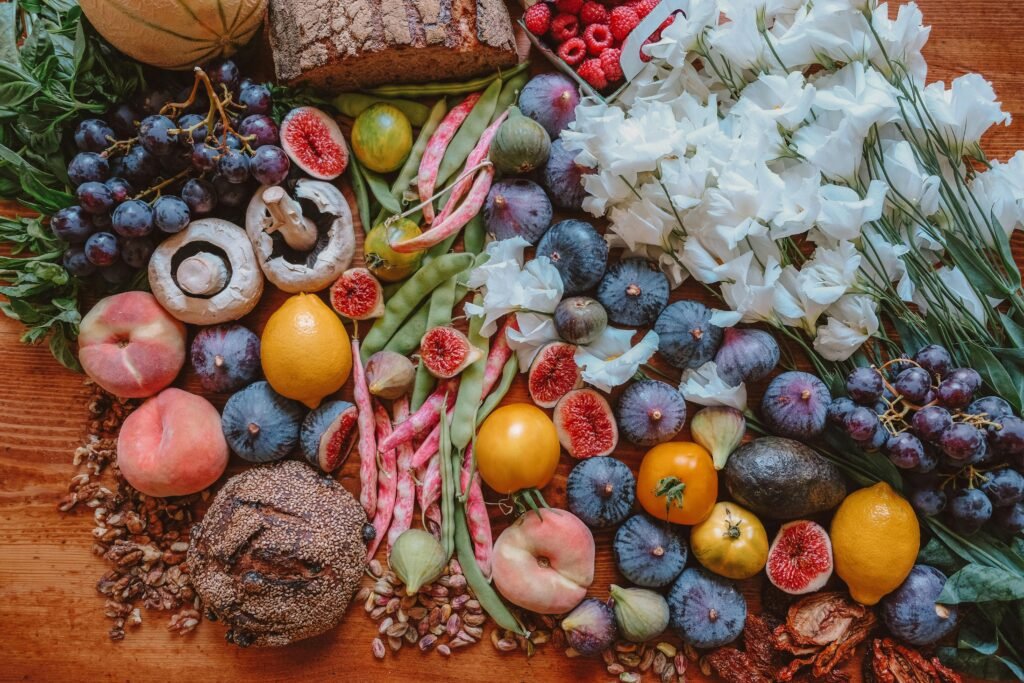 Frutas, verduras y flores sobre una mesa de madera.