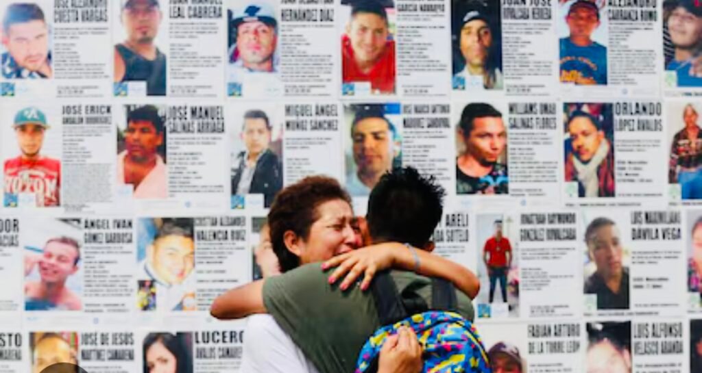 Personas abrazándose frente a carteles de desaparecidos.